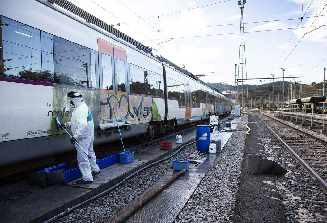 Un operario retira grafiti de un tren de cercanías en Barcelona.