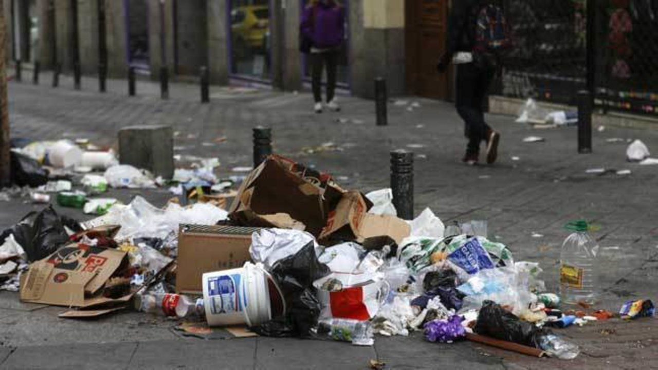 La basura y las hojas se amontonan en la acera y la calzada de una calle de Madrid.