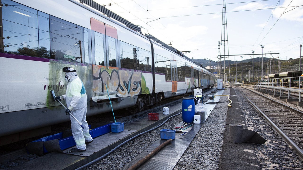 Un operario retira grafiti de un tren de cercanías en Barcelona.